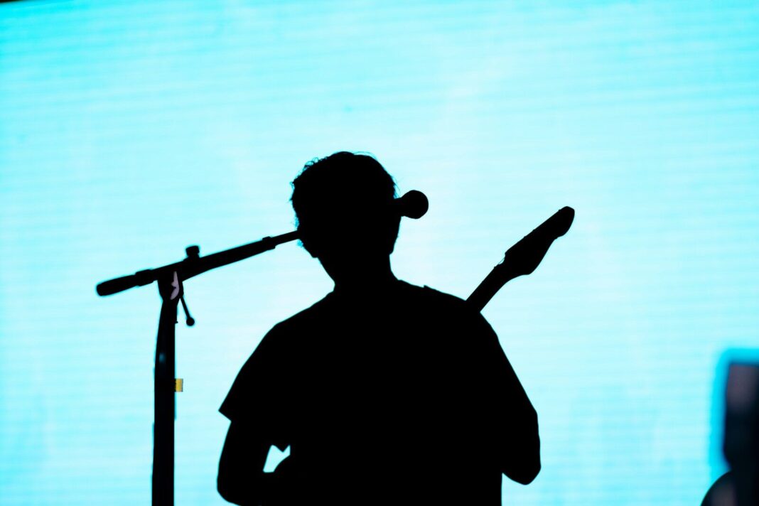 A musician plays guitar, silhouetted against light.